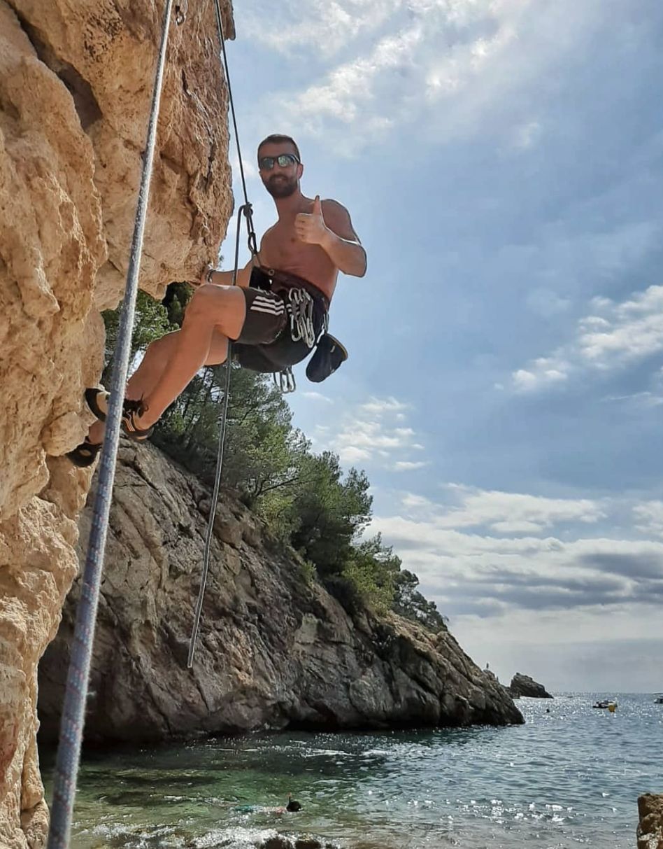 Matteo practica escalada en un acantilado junto al mar y levanta el pulgar