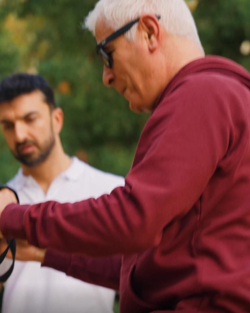 Matteo regola le cinghie per l’allenamento in sospensione con un cliente adulto all’aperto